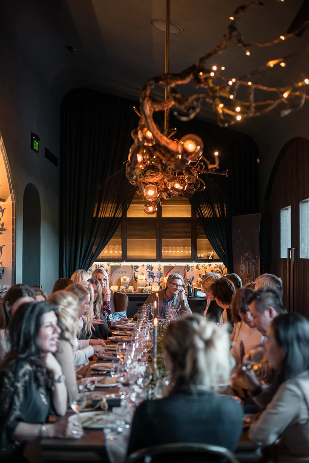 People sitting at a long table for a dinner party and chatting.