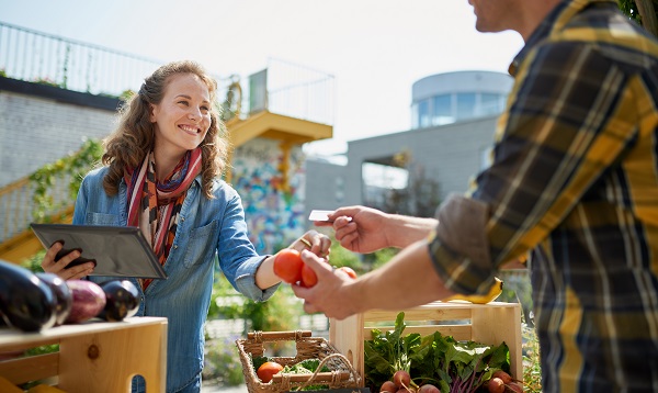 Female gardener selling organic crops and picking up a bountiful basket full of fresh produce