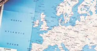 A map showcasing the north Atlantic ocean sits on top of the wooden table, next to a travel bag, and a phone.