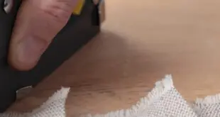 A closeup of a person's hand using a manual upholstery stapler to staple down the fabric to a rounded furniture.