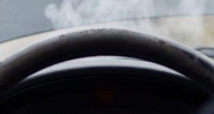 View from inside a car showing smoke rising from an open hood and a check engine light on the dashboard.
