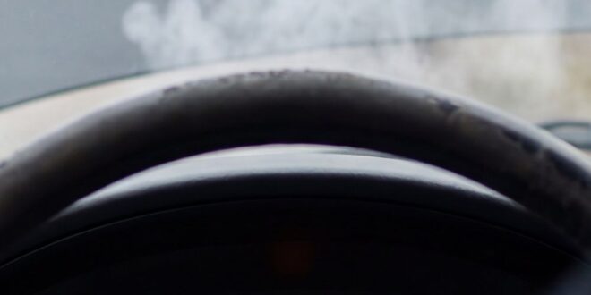 View from inside a car showing smoke rising from an open hood and a check engine light on the dashboard.