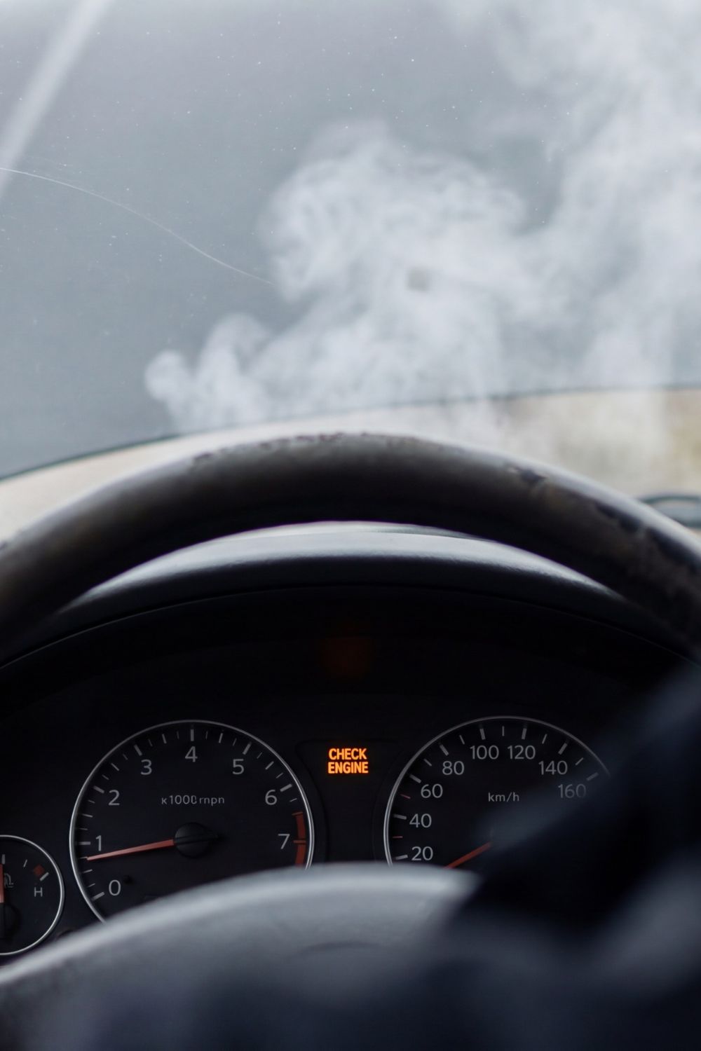 View from inside a car showing smoke rising from an open hood and a check engine light on the dashboard.