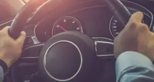 A person driving their car on the highway during the daytime. The sun is shining through the windshield of the car.