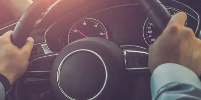 A person driving their car on the highway during the daytime. The sun is shining through the windshield of the car.