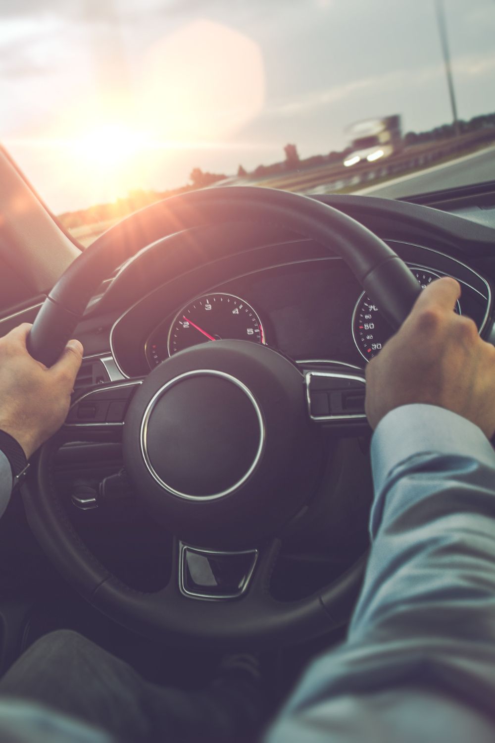 A person driving their car on the highway during the daytime. The sun is shining through the windshield of the car.