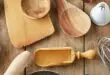 A variety of kitchen tools, including spoons, a whisk, cutters, and a rolling pin, are spread across a rustic table.