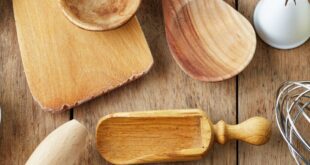 A variety of kitchen tools, including spoons, a whisk, cutters, and a rolling pin, are spread across a rustic table.