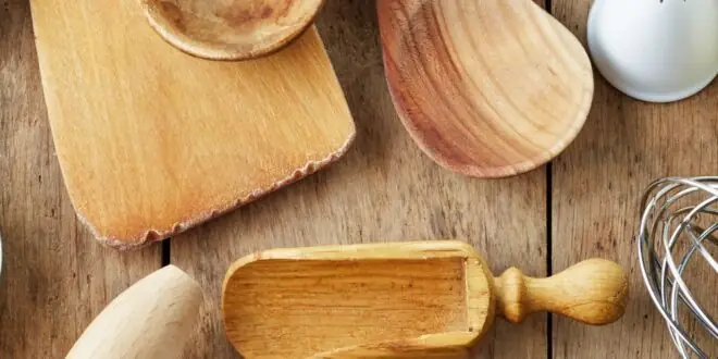 A variety of kitchen tools, including spoons, a whisk, cutters, and a rolling pin, are spread across a rustic table.