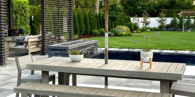 A large backyard with a pergola, table and chairs with an umbrella, a rectangular pool, and a concrete patio.
