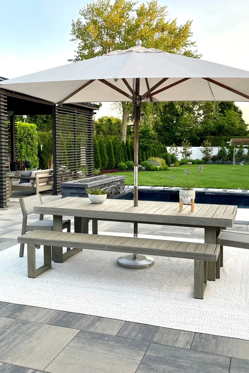 A large backyard with a pergola, table and chairs with an umbrella, a rectangular pool, and a concrete patio.
