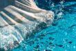 A close-up of a white pool skimmer moving through the surface of a home pool. The water is clear and healthy.