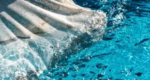 A close-up of a white pool skimmer moving through the surface of a home pool. The water is clear and healthy.