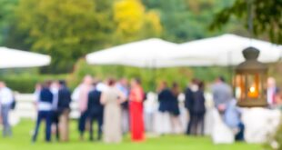 A close-up of a white lantern hanging from a tree with a blurry view of the wedding reception in the background.