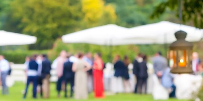 A close-up of a white lantern hanging from a tree with a blurry view of the wedding reception in the background.