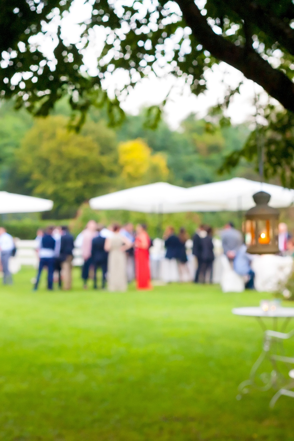 A close-up of a white lantern hanging from a tree with a blurry view of the wedding reception in the background.
