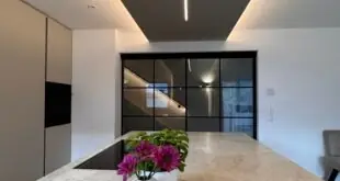 A long kitchen island has a brown and gray stone countertop. A circular tray with floral vases is on the counter.