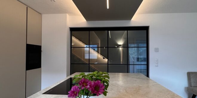 A long kitchen island has a brown and gray stone countertop. A circular tray with floral vases is on the counter.