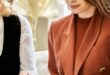 Three professionally dressed women look through an open portfolio together in a bright, stylish indoor setting.
