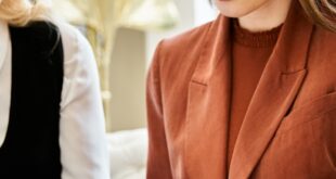 Three professionally dressed women look through an open portfolio together in a bright, stylish indoor setting.