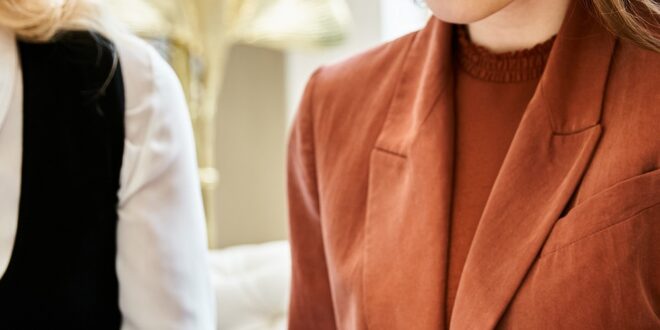 Three professionally dressed women look through an open portfolio together in a bright, stylish indoor setting.