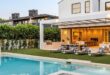 A modern white two-story home with a backyard swimming pool, raised spa, green lawn, and covered outdoor seating area.