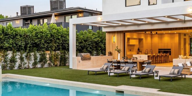 A modern white two-story home with a backyard swimming pool, raised spa, green lawn, and covered outdoor seating area.